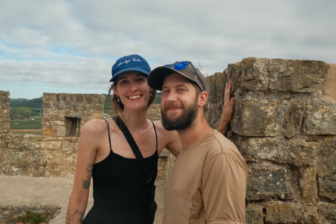 Two people standing in front of a stone wall with a scenic background
